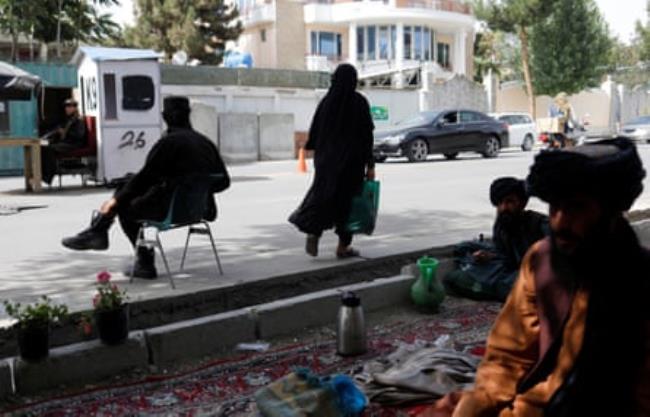 An Afghan woman walks among Taliban soldiers at a checkpoint in central Kabul, July 2023.
