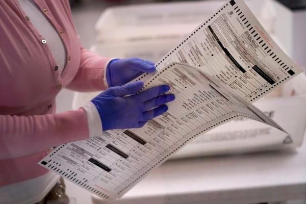 An election worker carries two ballots to be verified inside the Maricopa County Recorders Office, Nov. 10, 2022, in Phoenix.