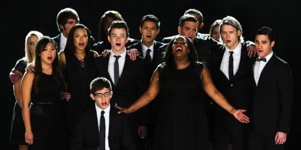 The cast of Glee dressed in white and black and are singing emotionally